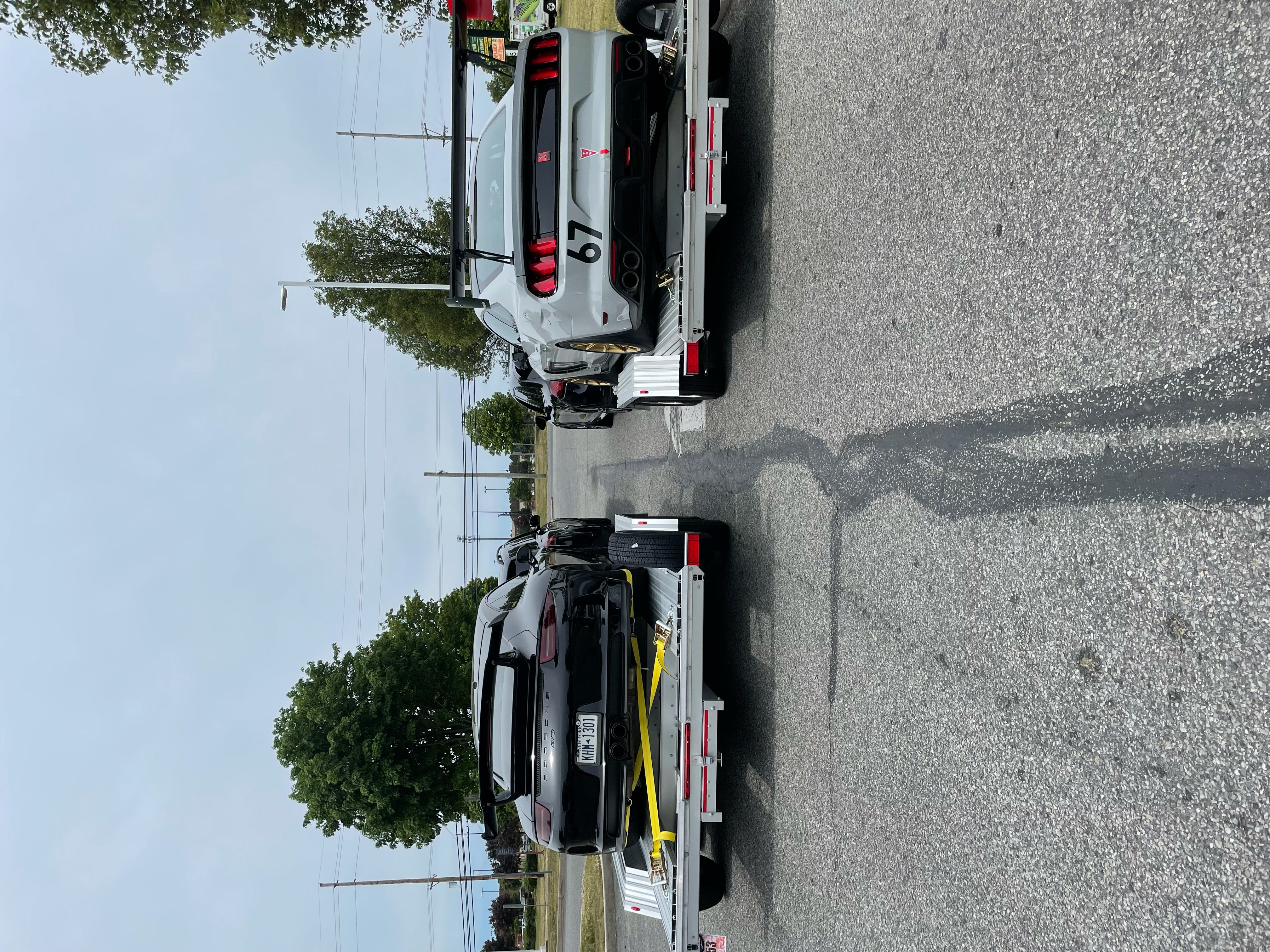Porsche GT3 and Ford Mustang loaded on two open trailers side by side